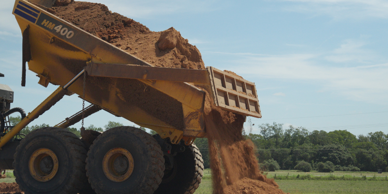 Articulated dump truck unloading dirt during metal building site preparation.